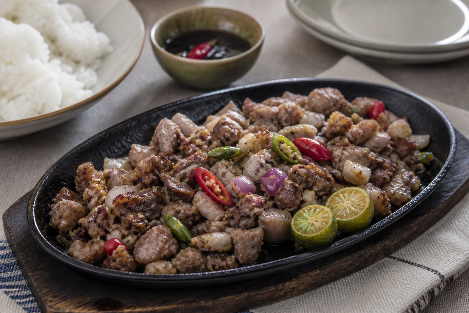 Filipino pork sisig with onions, chilies, and calamansi on a sizzling platter.