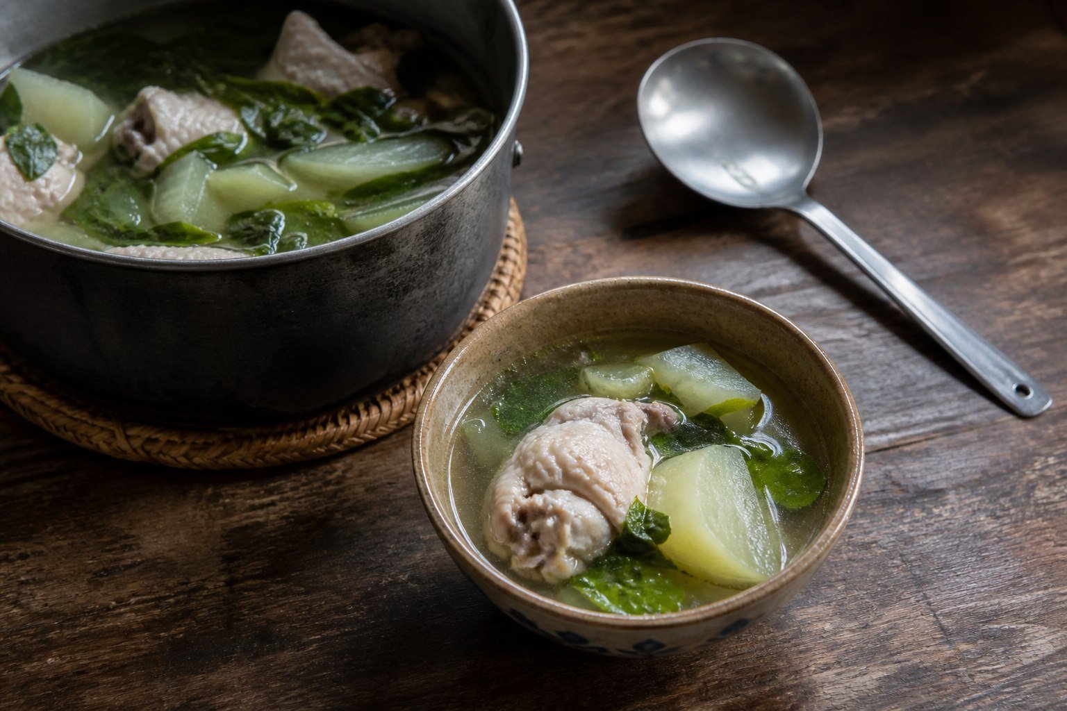 A bowl of chicken tinola served beside the cooking pot and ladle.