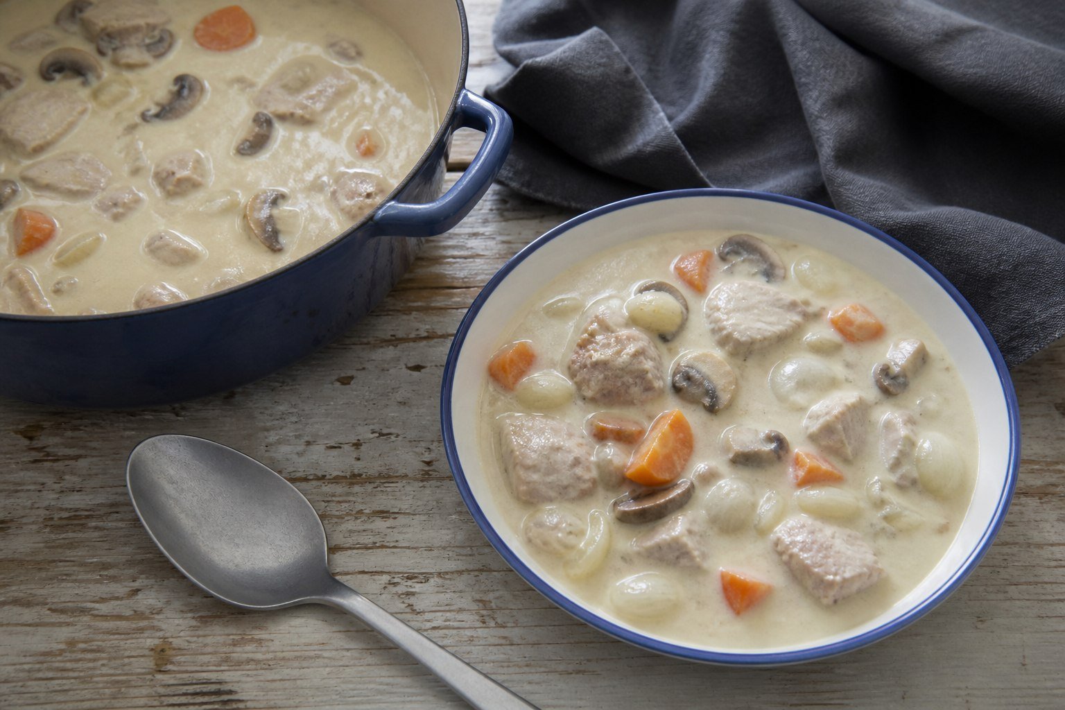 A bowl of French veal blanquette beside the enameled casserole.