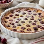 A rustic French cherry clafoutis dusted with powdered sugar in a white baking dish.