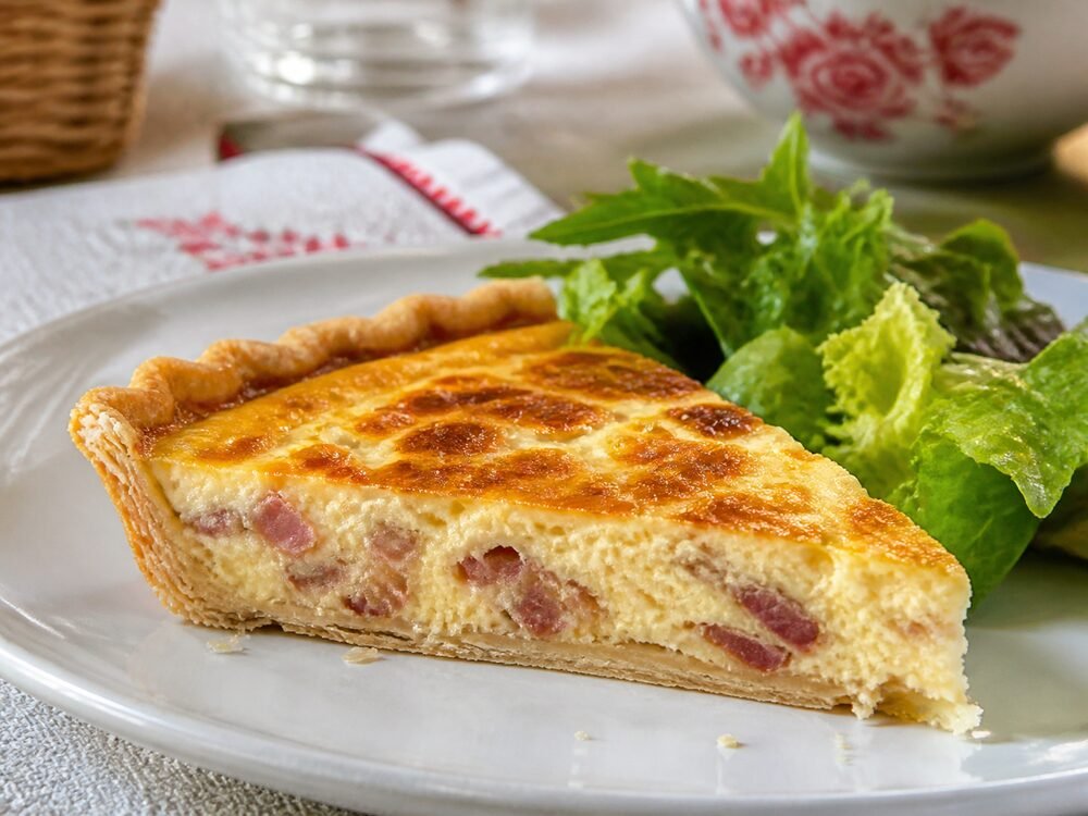 A slice of quiche Lorraine showing flaky pastry, creamy custard, and browned bacon.