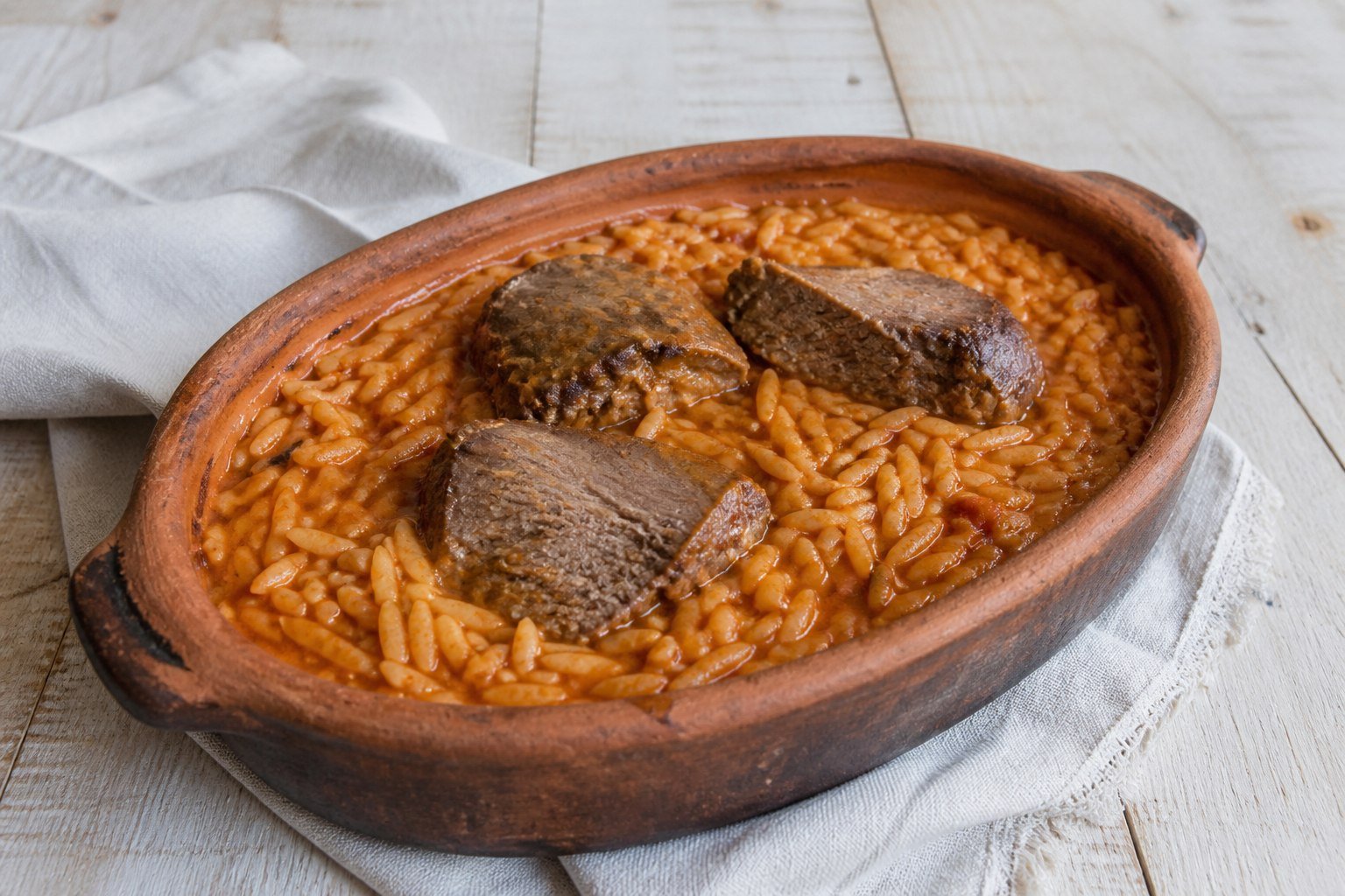 Greek giouvetsi with tomato-braised beef, orzo, and grated cheese in terracotta.