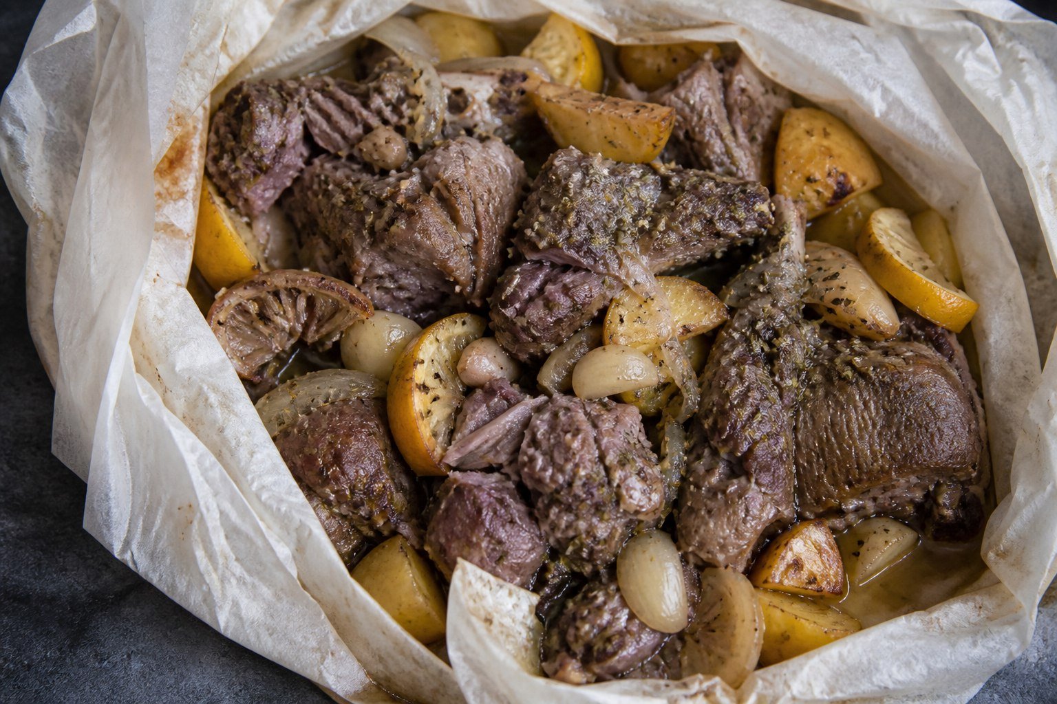 Tender lamb shoulder, lemon, garlic, and potatoes inside a parchment parcel.