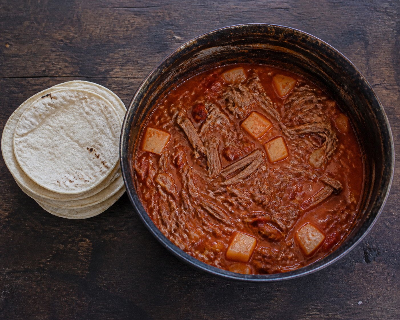 Guatemalan hilachas simmering in a pot beside corn tortillas.