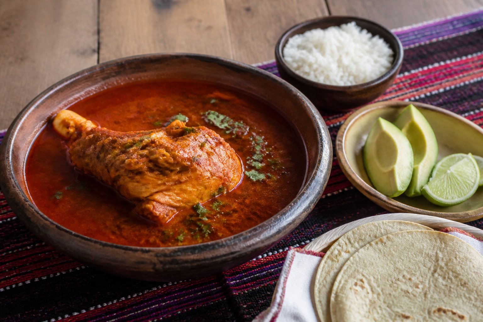 Guatemalan Kak'ik red turkey soup with rice, avocado, lime, and tortillas.