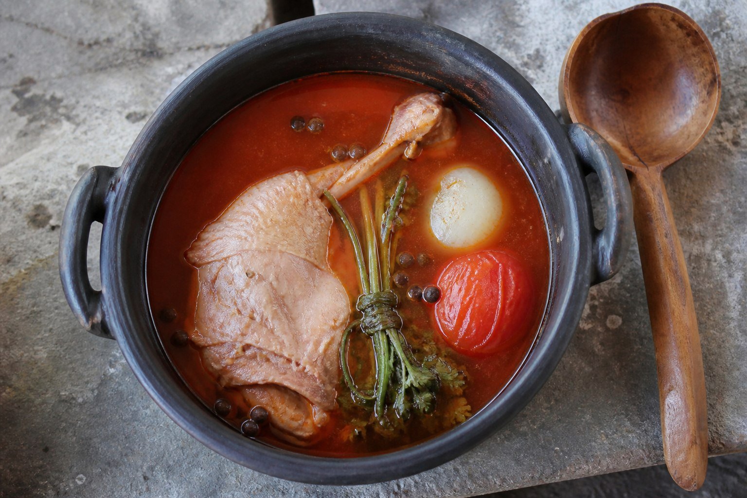 Turkey simmering in a clay pot of red Kak'ik broth with tomato, spices, and herbs.
