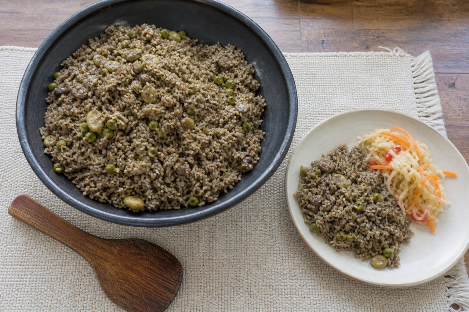 Haitian mushroom rice being served from a dark communal bowl beside bright pikliz.