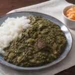 Haitian legim vegetable stew with beef, served beside white rice and pikliz.