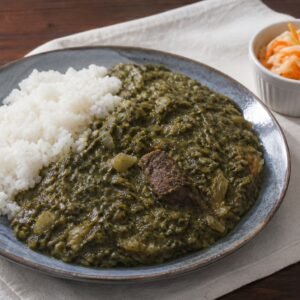 Haitian legim vegetable stew with beef, served beside white rice and pikliz.