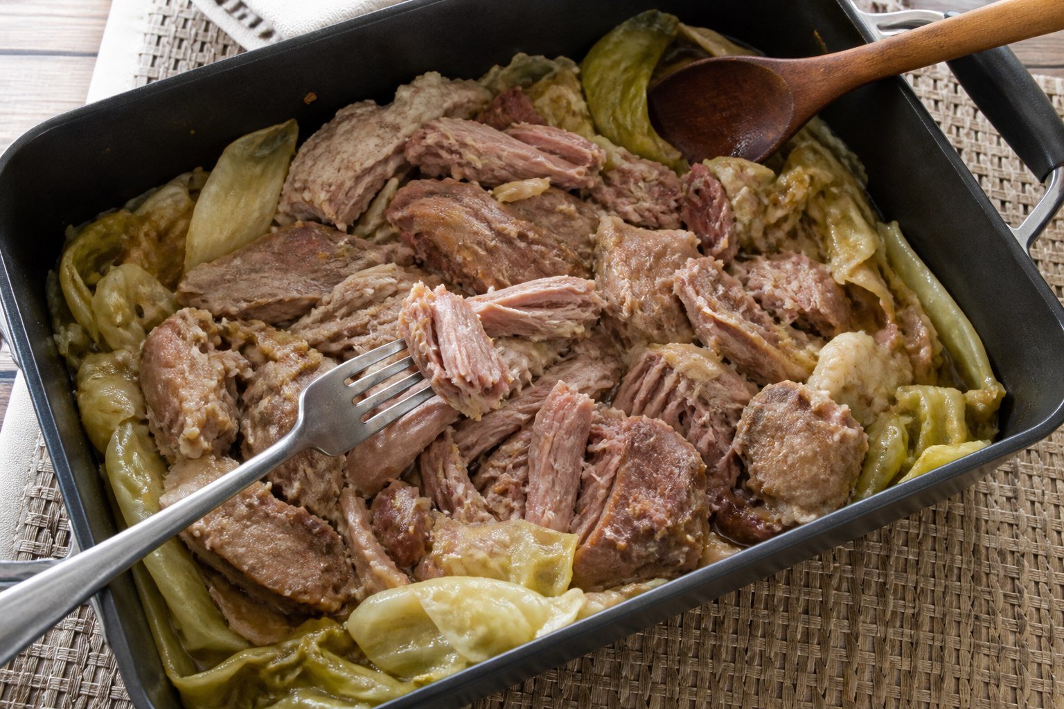 Tender kalua pork pulled into irregular pieces in a cabbage-lined roasting pan.