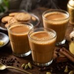 Steaming Indian masala chai in glass cups with cardamom, cinnamon, ginger, and cloves.