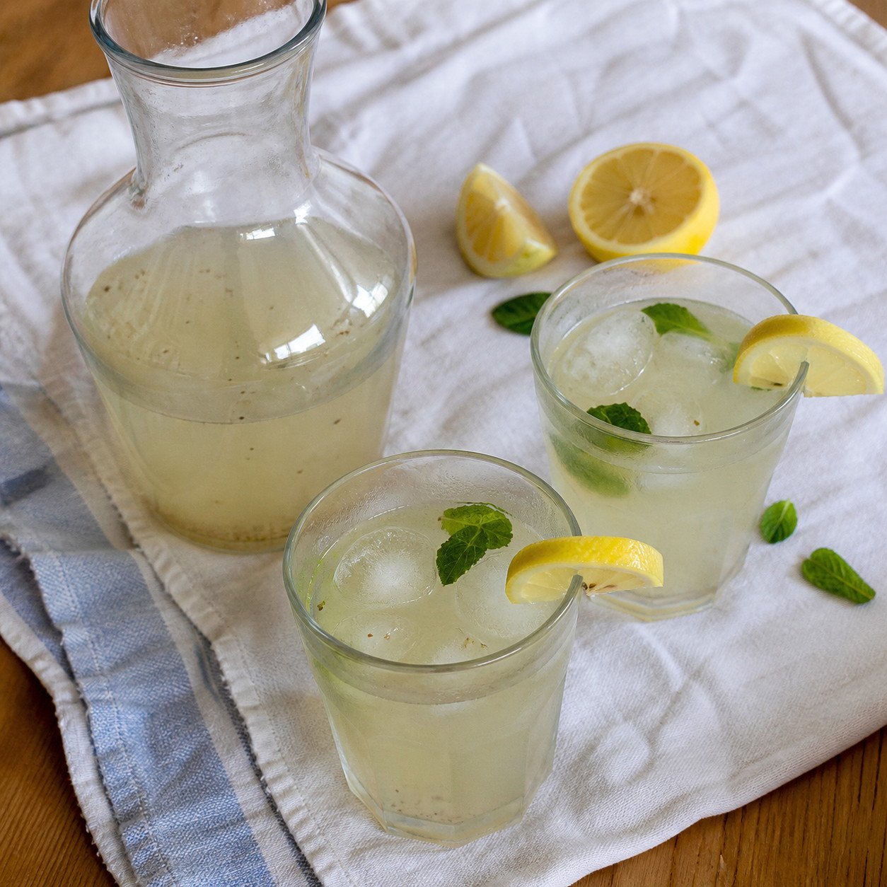 A carafe and two glasses of Indian nimbu pani with ice and mint.