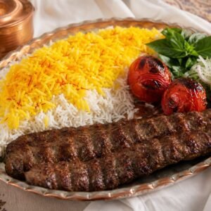 Iranian chelo kebab with charred beef kebab, saffron basmati rice, grilled tomatoes, lemon, and herbs.