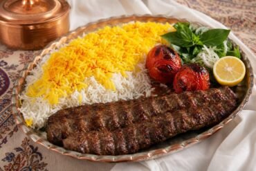 Iranian chelo kebab with charred beef kebab, saffron basmati rice, grilled tomatoes, lemon, and herbs.