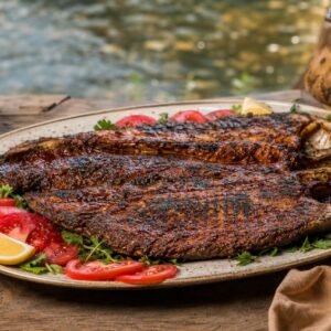 Iraqi Masgouf grilled carp with tamarind glaze, herbs, tomatoes, and lemon.