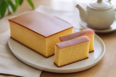 A tall loaf of Japanese castella cake with a smooth brown top and fine golden crumb.