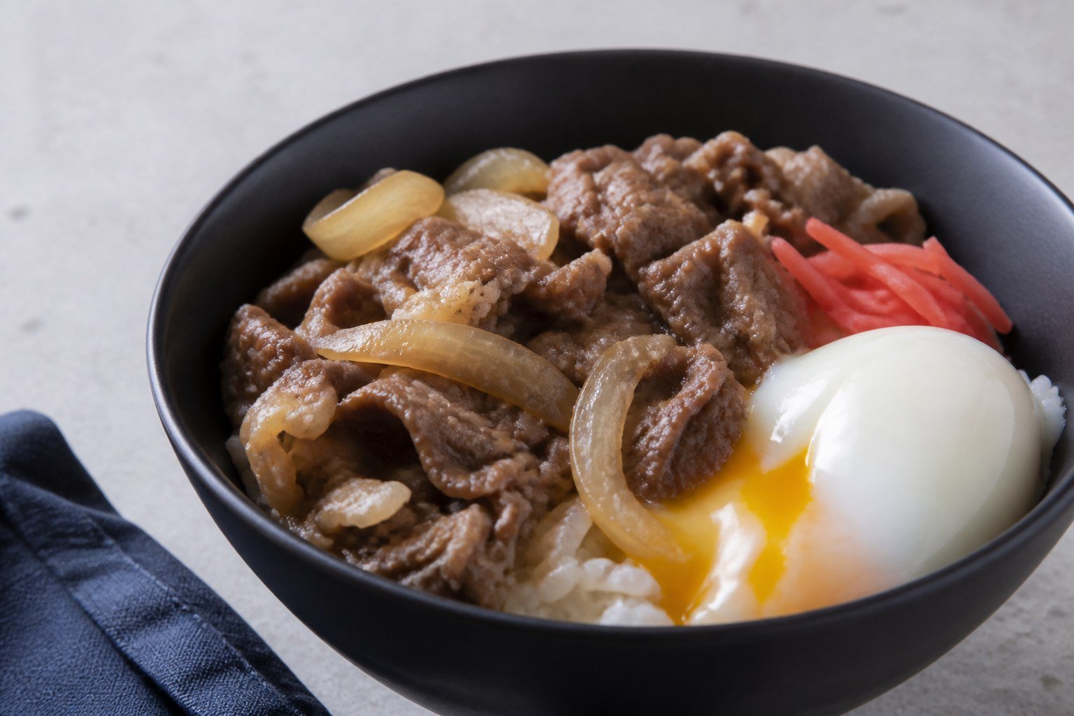 Close bowl of gyudon topped with a soft egg and pickled ginger.