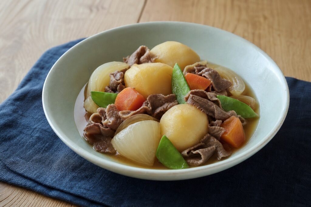 Japanese nikujaga with thin beef, potatoes, onions, carrots, and snow peas in dashi broth.