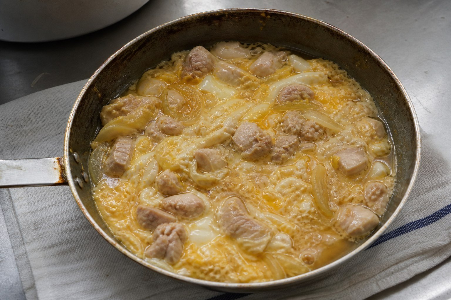 Chicken, onion, and softly set egg simmering in a skillet for Japanese oyakodon.