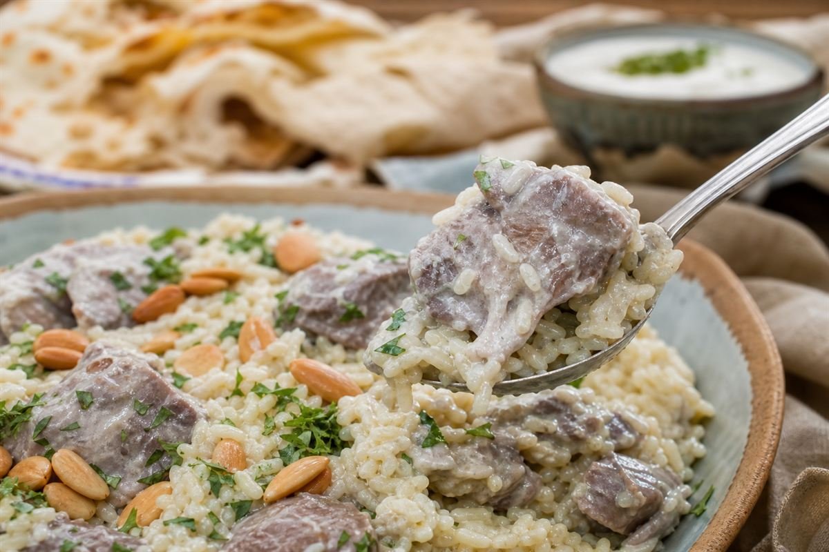 A spoonful of Jordanian mansaf showing lamb and rice coated in creamy sauce.
