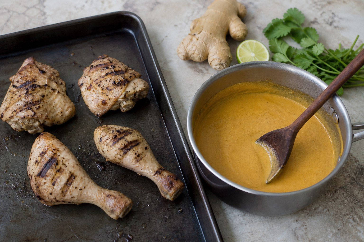 Grilled chicken pieces beside smooth coconut tomato sauce before finishing Kenyan kuku paka.