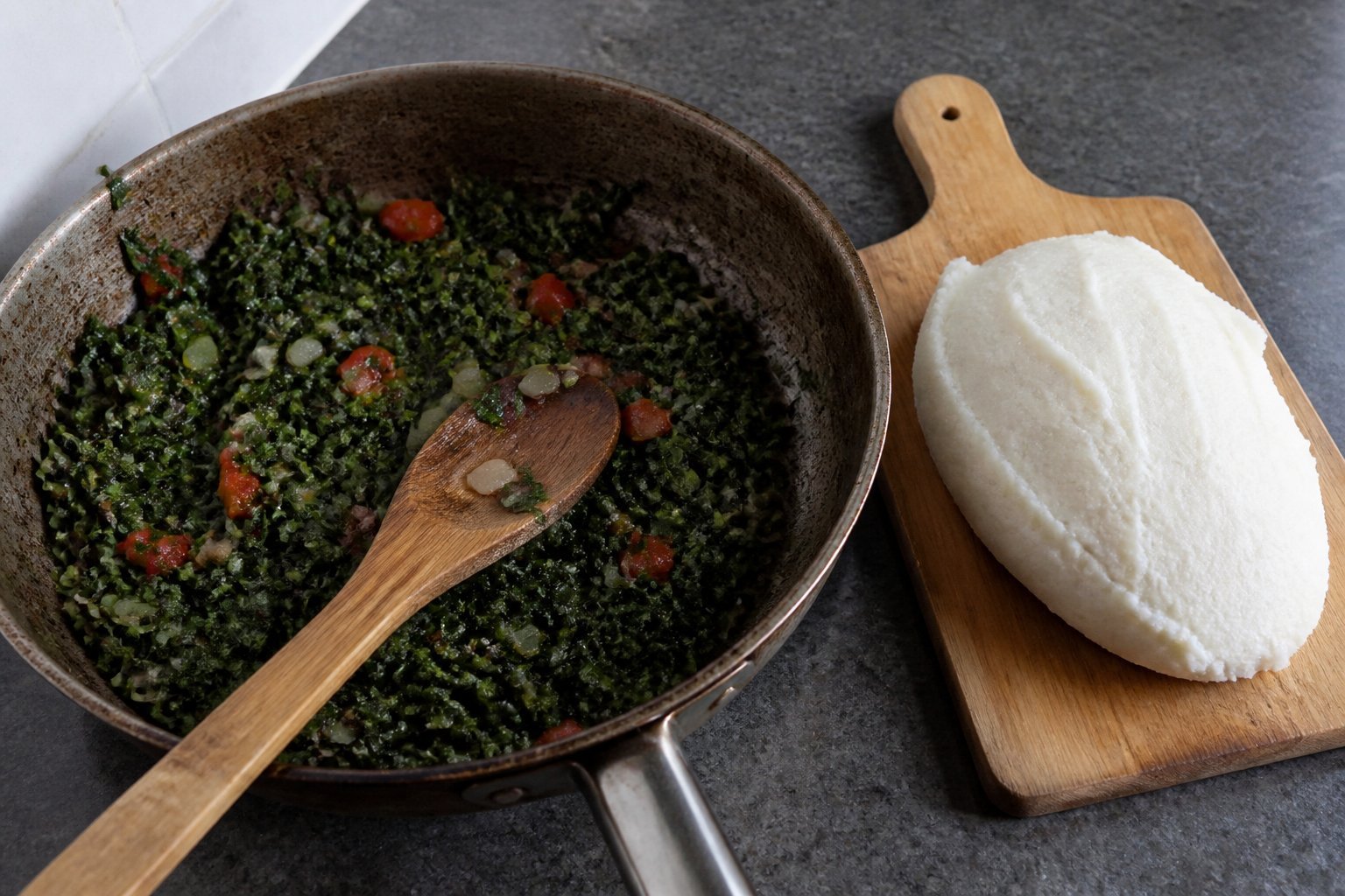 Sukuma wiki cooking in a skillet beside a smooth portion of Kenyan maize ugali.