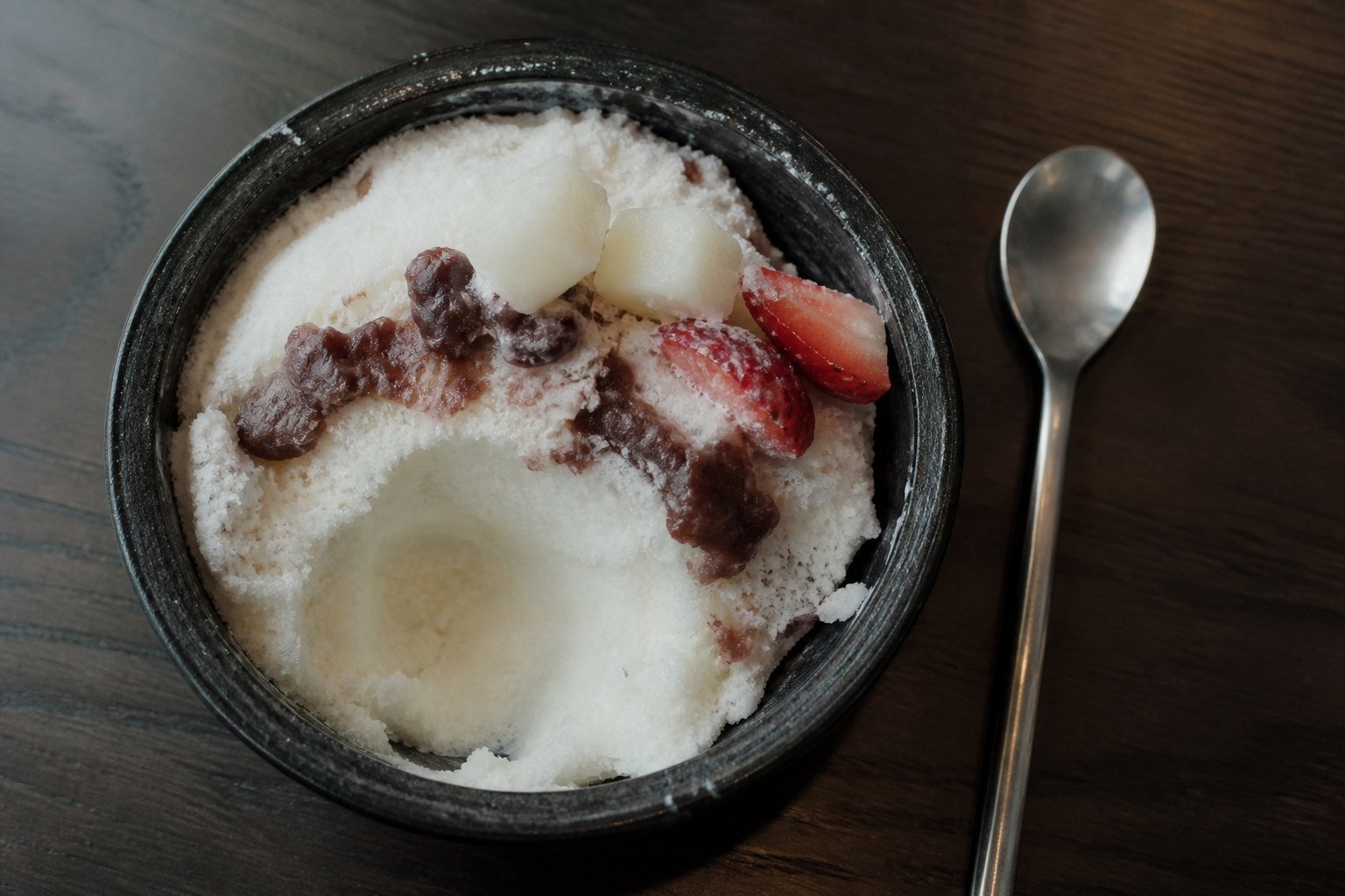 A spoonful taken from patbingsu reveals softly melting milk ice beneath red bean paste and fruit.