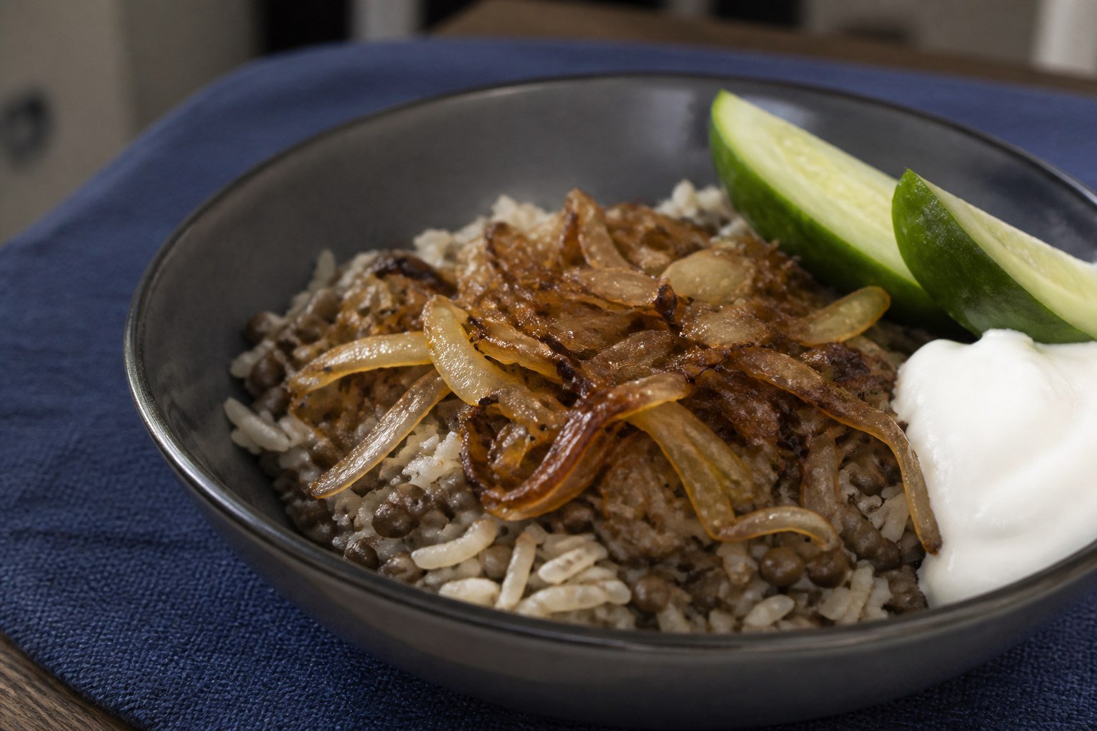 A bowl of mujadara with caramelized onions, yogurt, and cucumber.