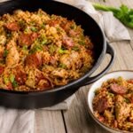Chicken and sausage jambalaya served in a cast-iron pot with a bowl alongside.