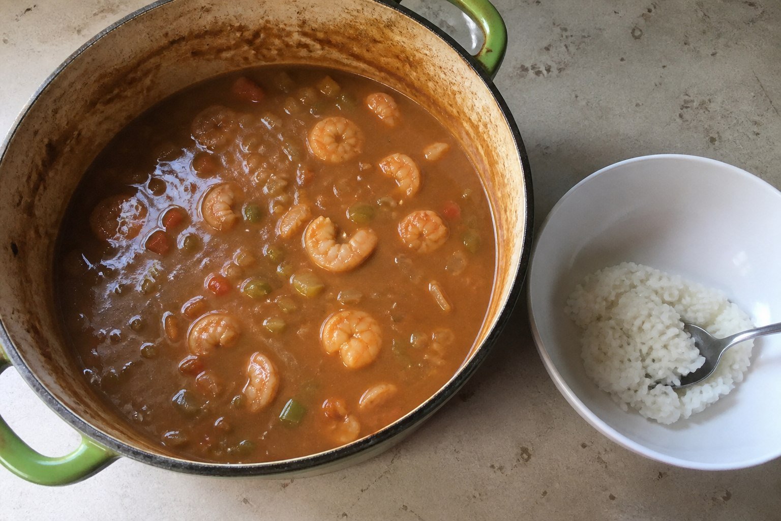 Shrimp etouffee in an enamel pot beside a bowl of white rice.