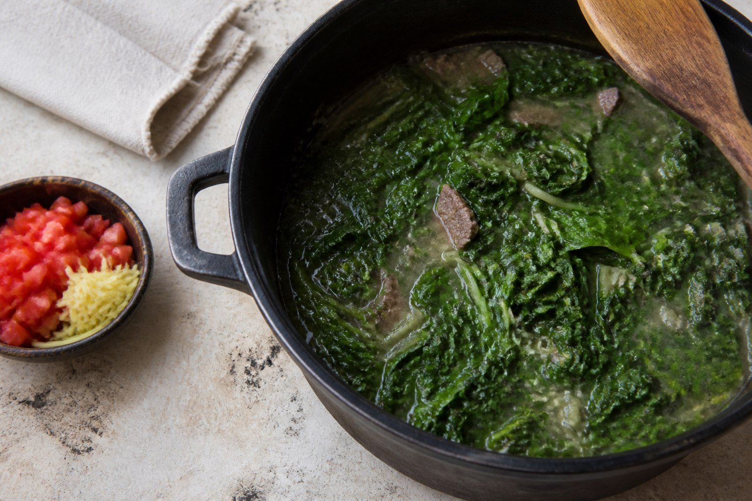 Mixed leafy greens wilting into a pot of Malagasy beef romazava.