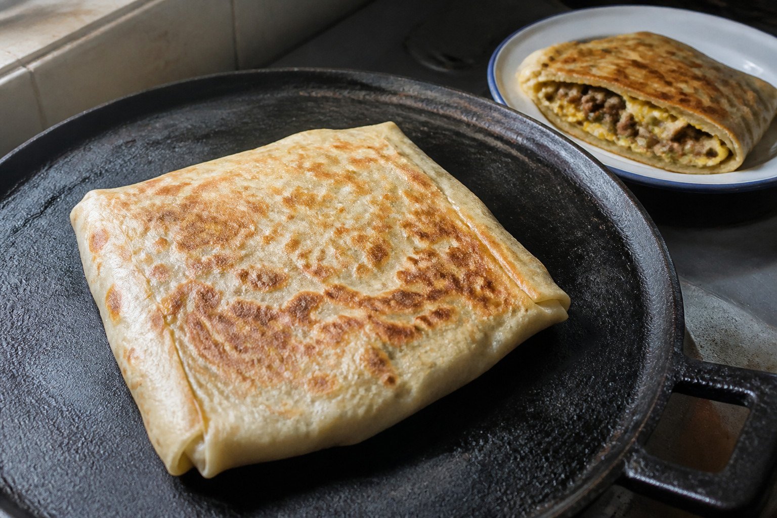 A whole Malaysian murtabak cooking on a cast-iron griddle.