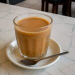 Glass of Malaysian teh tarik pulled milk tea on a kopitiam-style table.