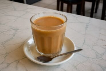 Glass of Malaysian teh tarik pulled milk tea on a kopitiam-style table.