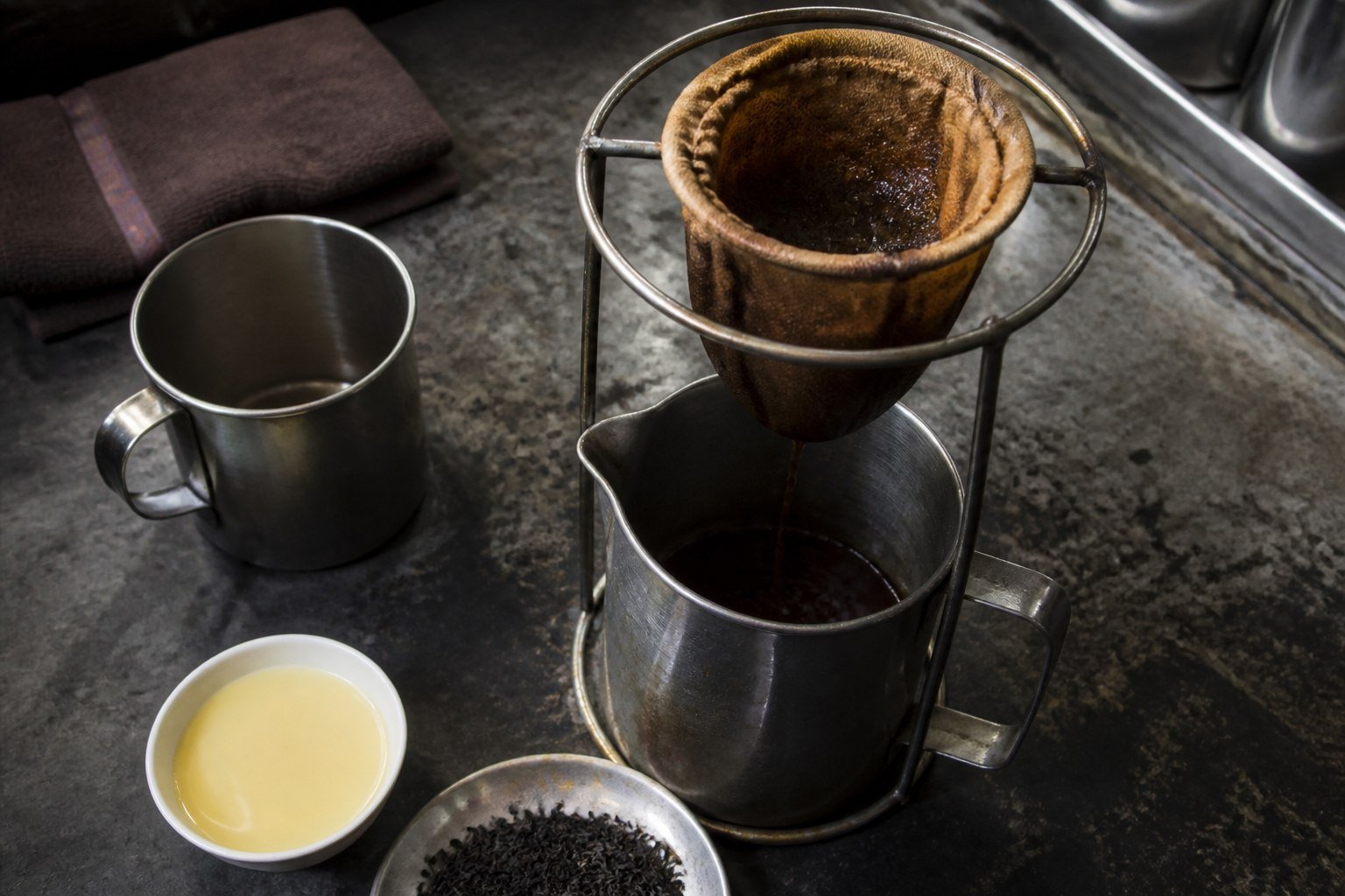 Black tea dripping through a cloth filter into a metal pitcher for Malaysian teh tarik.