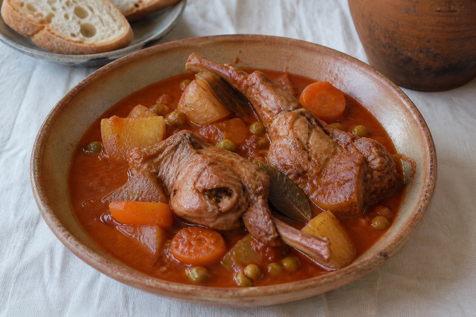 Maltese stuffat tal-fenek rabbit stew with tomato, red wine, potatoes, carrots, peas, and bread.