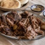 Moroccan mechoui lamb torn into large tender pieces and served with bread, cumin, and salt.
