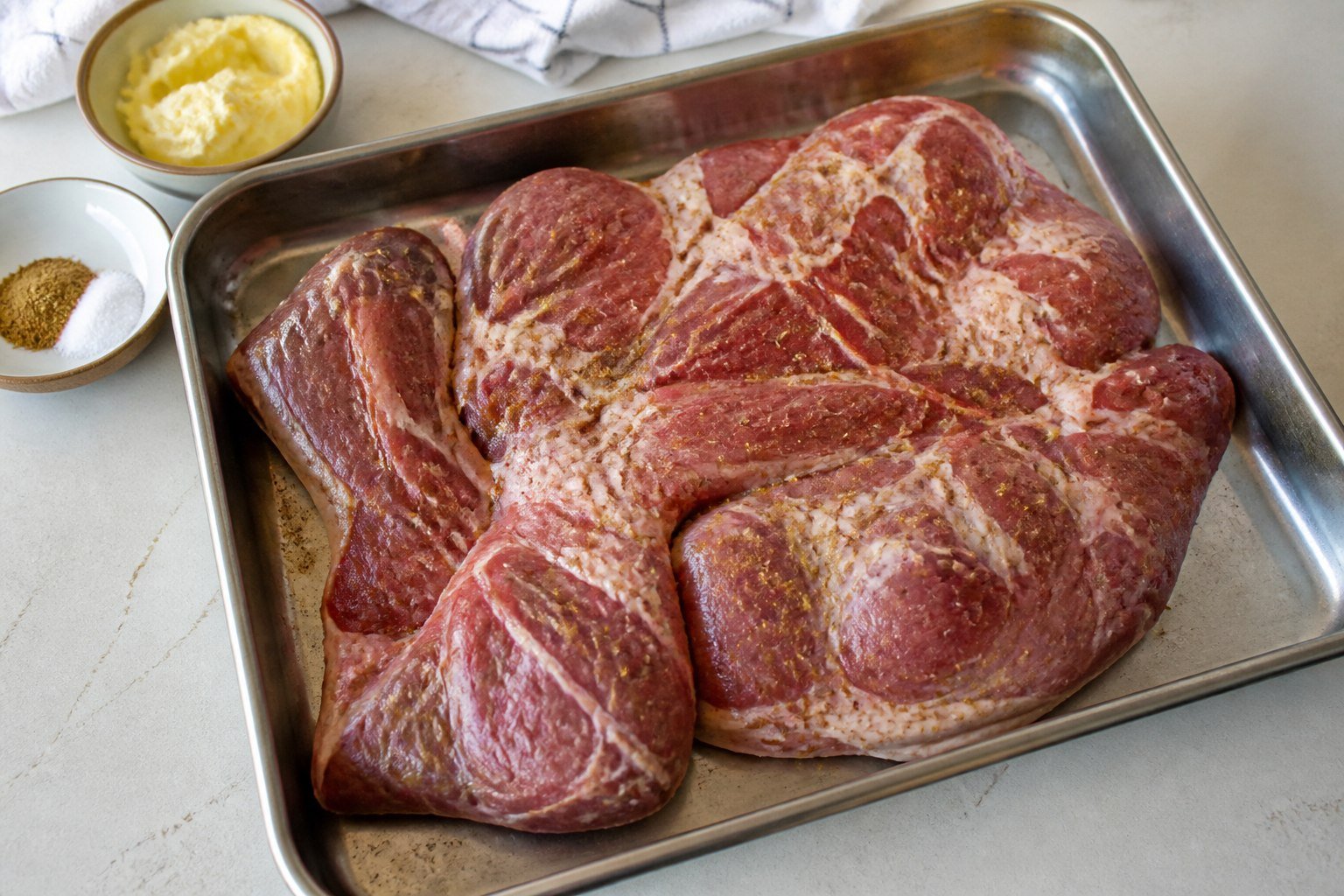 Raw boneless lamb shoulder seasoned in a roasting pan for Moroccan mechoui.