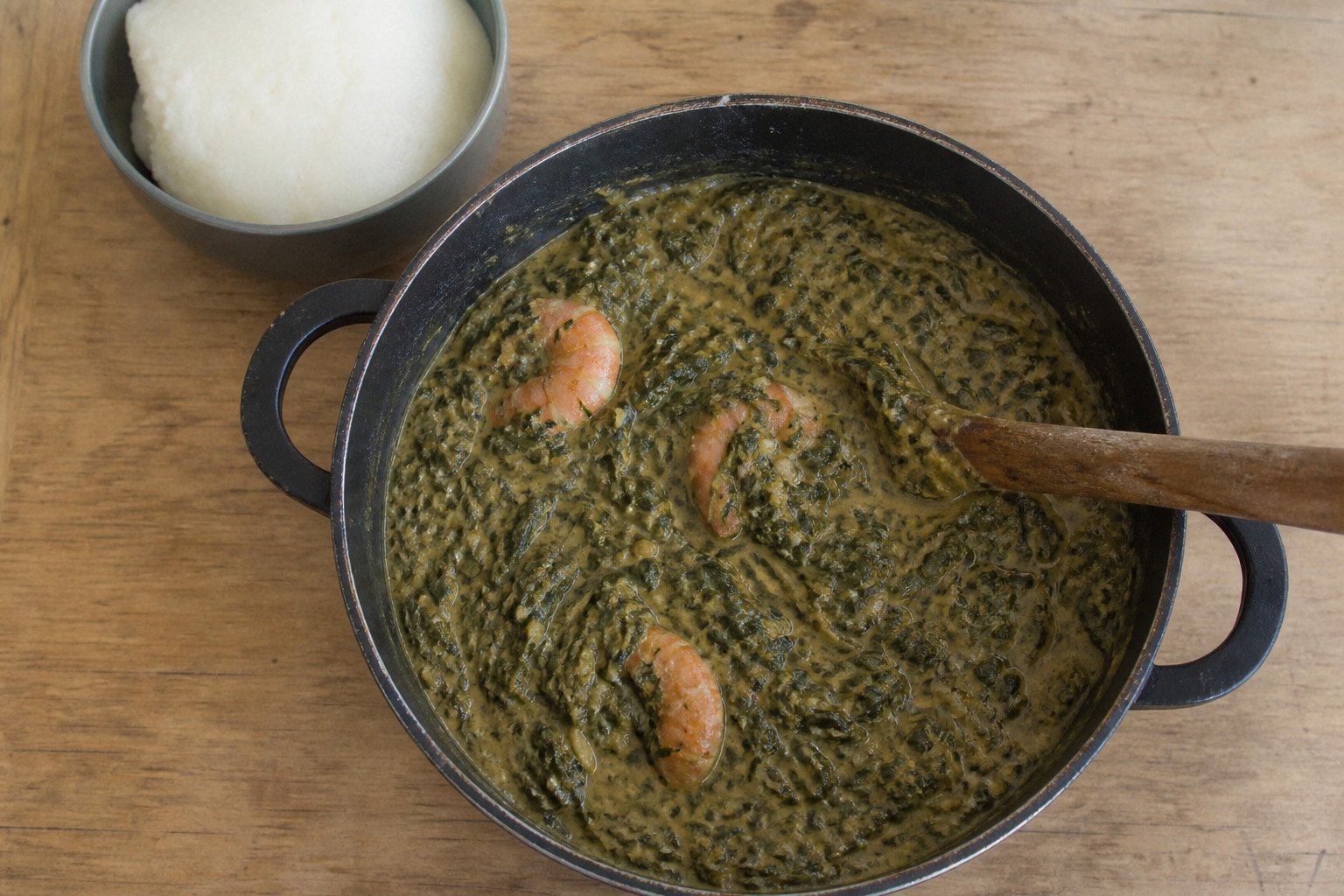 Mozambican matapa simmering in a pot with a wooden spoon.