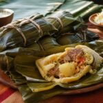 Nicaraguan nacatamales wrapped in banana leaves, with one opened to show pork, masa, potato, rice, and vegetables.