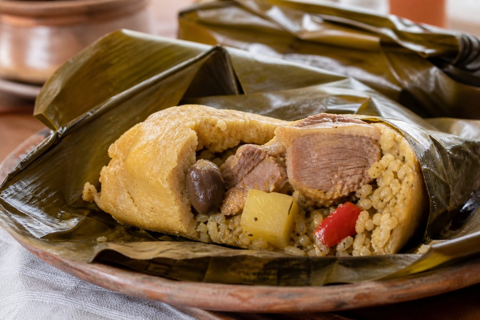 An opened Nicaraguan nacatamal showing tender pork and vegetables inside soft corn masa and banana leaves.