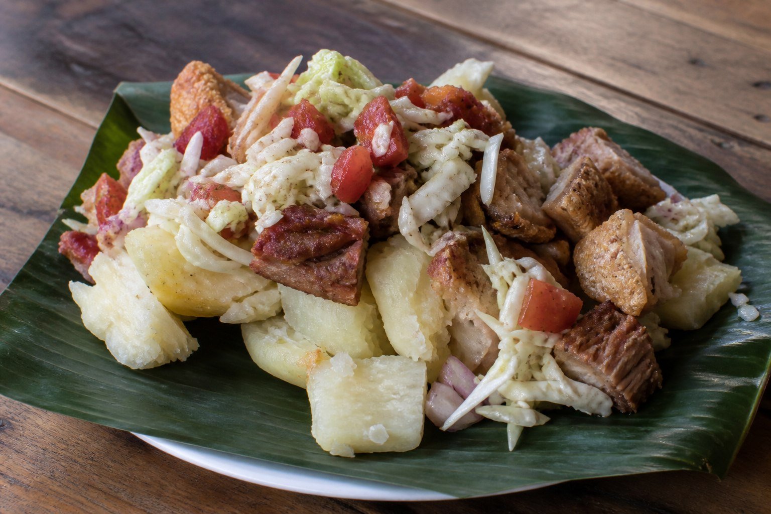 Nicaraguan vigorón with boiled yuca, chicharrón, and cabbage curtido on a banana leaf.