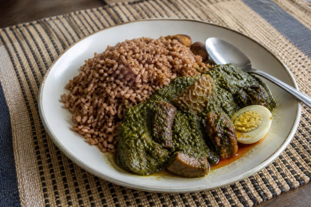 Nigerian Ofada rice with green ayamase pepper stew, beef, tripe, boiled egg, and palm oil.