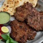 Pakistani chapli kebab with naan, tomato, onion, lemon, and mint chutney.