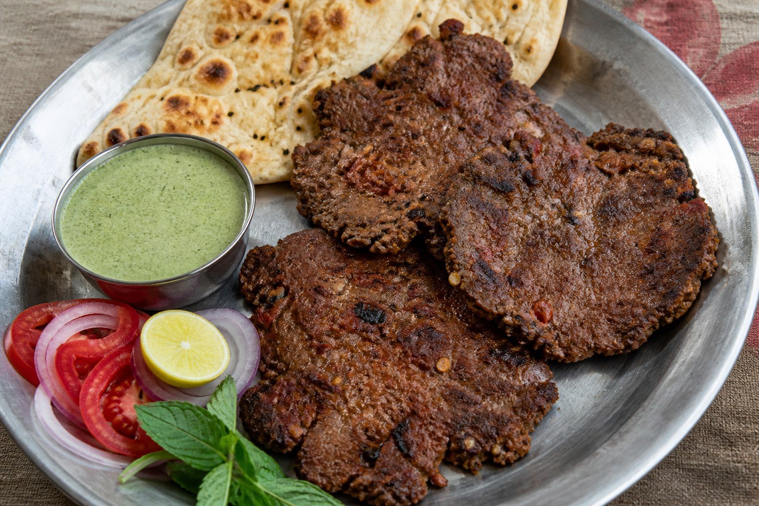 Pakistani chapli kebab with naan, tomato, onion, lemon, and mint chutney.