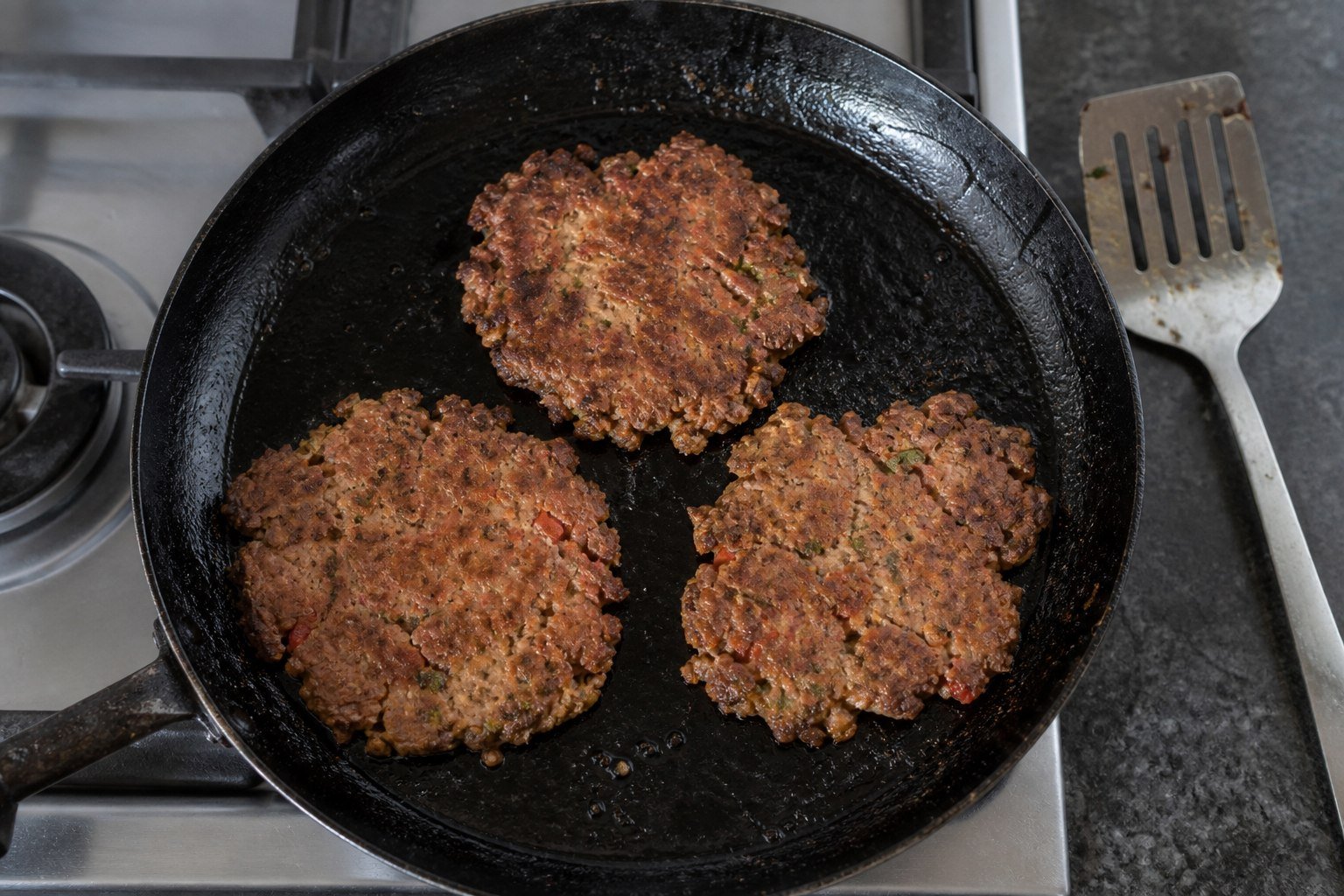 Thin chapli kebab patties cooking in a cast-iron skillet.