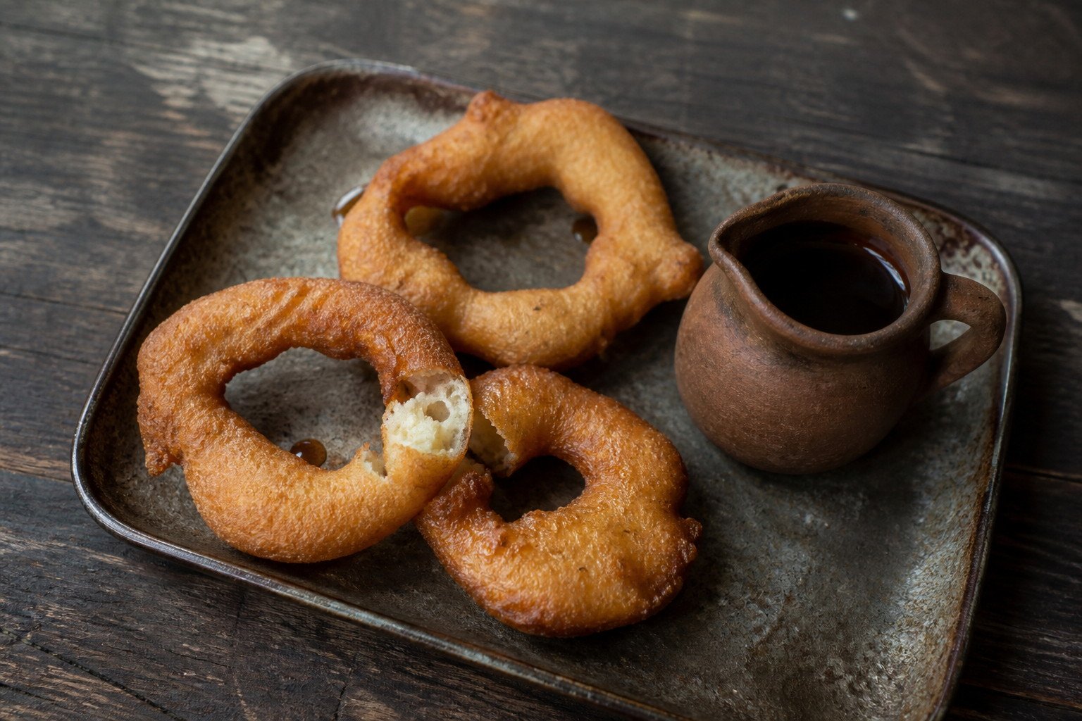 Hand-shaped Peruvian picarones with a small pitcher of chancaca syrup.