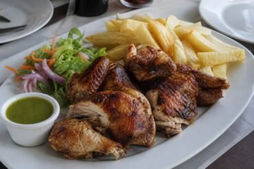 Peruvian pollo a la brasa served with fries, salad, and green aji sauce.