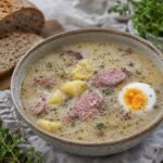 Polish żurek sour rye soup with smoked sausage, potatoes, boiled egg, and rye bread.