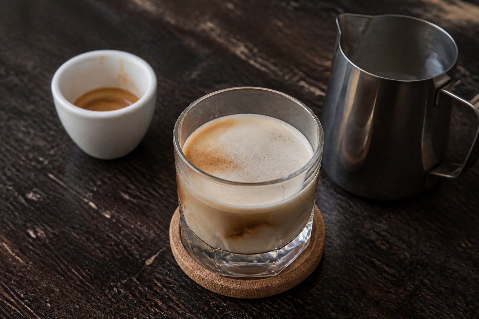 Espresso, hot milk pitcher, and a short glass of freshly mixed galão.